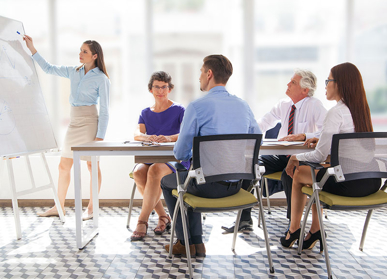 People in meeting room around table looking at board, taking part in training and development using our HR and Payroll Outsourcing solution