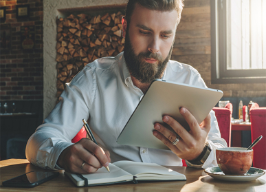 Man writing in notebook and looking at tablet