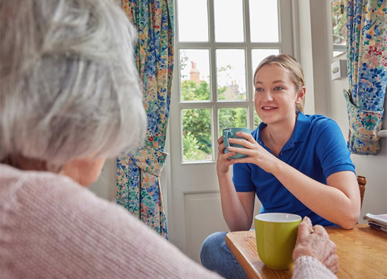 Care home employee and resident having a cup of tea and chatting